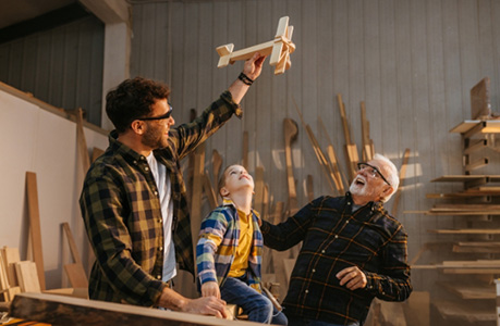 Dad entertaining son with toy wooden airplane while grandfather watches