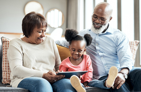 Grandparents sitting on couch with granddaughter and reading